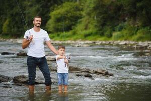 A father teaching his son how to fish on a river outside in summer sunshine. father's day. photo