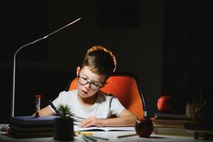 Boy learn lessons in the home setting at the table in the light of a table lamp. photo