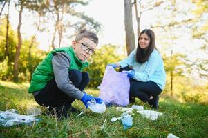 Mom teaches her son to clean up trash in nature. A woman removes plastic bottles in a bag. The topic of environmental pollution by garbage. photo