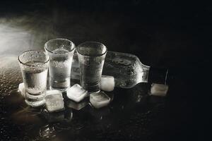 Close-up view of bottle of vodka with glasses standing on ice on black. photo