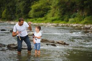 A father teaching his son how to fish on a river outside in summer sunshine. father's day. photo