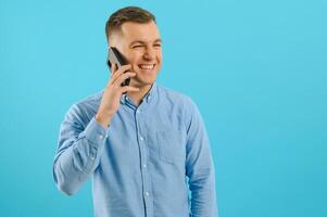 Young man in bright colorful wear talking on mobile cell phone on blue background. Trendy guy have conversation. Smartphone, technology concept. photo