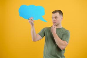 Cheerful young male pointing up and holding empty speech bubble with blank space for quote against vivid yellow background photo