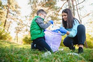 Smiling boy picking up trash in the park with his mother. Volunteer concept. photo