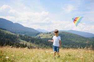 Little boy running on a background of mountains with kite. Sunny summer day. Happy childhood concept. photo