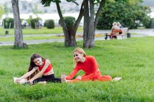 madre y hija haciendo yoga ejercicios en césped en el parque a el día tiempo. personas teniendo divertido al aire libre. concepto de simpático familia y de verano vacaciones. foto