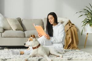 un hermosa joven mujer leyendo su favorito libro con su perro. foto