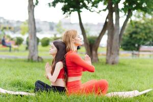 Mother and daughter doing yoga exercises on grass in the park at the day time photo