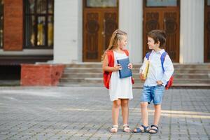 Happy children - boy and girl with books and backpacks on the first school day. Excited to be back to school after vacation. Full length outdoor portrait. photo