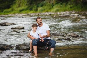 A father teaching his son how to fish on a river outside in summer sunshine photo