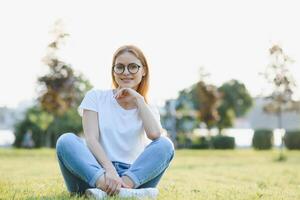 Stylish young woman spends time in the park on the green grass. summer vacation concept. photo