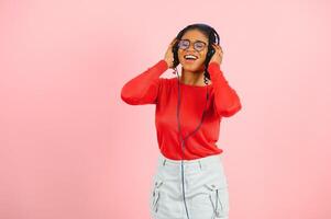 Pretty african american young woman with bright smile dressed in casual clothes, glasses and headphones dance over pink background photo