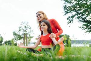 Mother and daughter doing yoga exercises on grass in the park at the day time. People having fun outdoors. Concept of friendly family and of summer vacation. photo