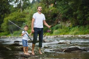 A father teaching his son how to fish on a river outside in summer sunshine photo