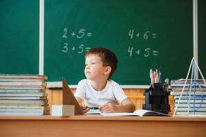 Back to school. A schoolboy is reading a book while sitting at the table for the first time at school on the background of the school blackboard. photo