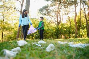 Smiling boy picking up trash in the park with his mother. Volunteer concept. photo