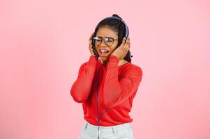 Beautiful woman with afro hair listining to music and dancing on pink background. photo