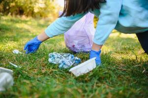 De las mujeres manos en rojo caucho guantes. mujer recoge basura en el bolsa. voluntario Hurgar basura en el verano parque. bonito progresivo mujer haciendo un esfuerzo a ayuda el ambiente foto