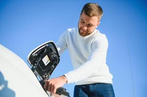 Man charges an electric car at the charging station photo