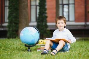 Pupil near school. Boy sitting with a book. photo