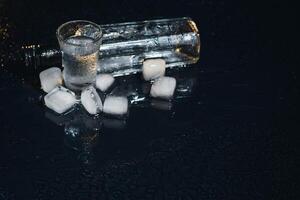 Close-up view of bottle of vodka with glasses standing on ice on black. photo