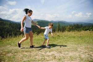 The boy and his mother are standing on the top of the mountain. A woman is traveling with child. Boy with his mother looking at the mountains. Travel with backpacks. Hike and climb with kids. photo