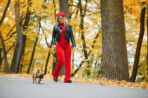 a stylish young girl with long light hair in sunny glasses goes for a walk with a little middle doggy a pug by the French bulldog in a park in spring in autumn photo