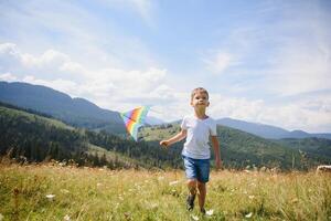 Little boy running on a background of mountains with kite. Sunny summer day. Happy childhood concept. photo