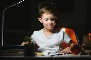 Boy learn lessons in the home setting at the table in the light of a table lamp. photo