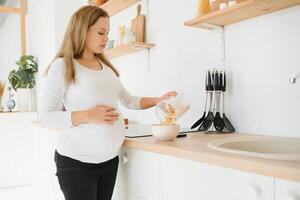 embarazada mujer preparando desayuno, cereales con Leche y natural jugo, en el cocina. foto