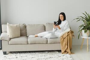 retrato de un alegre joven mujer utilizando móvil teléfono mientras relajante en un sofá a hogar. foto