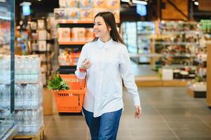 sale, shopping, consumerism and people concept - woman with food basket at grocery store or supermarket photo