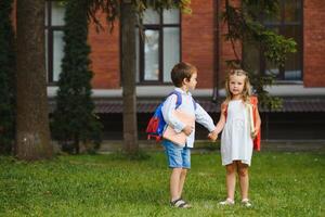 Happy children go back to school. Pupil of primary school go study with backpack outdoors. Kids go hand in hand. Beginning of lessons. First day of fall. Boy and girl from elementary student. photo