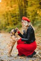 a stylish young girl with long light hair in sunny glasses goes for a walk with a little middle doggy a pug by the French bulldog in a park in spring in autumn photo