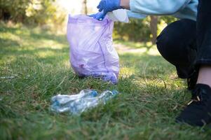 mano pone el plastico escombros en el basura bolso en el parque foto