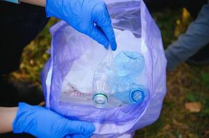 mano pone el plastico escombros en el basura bolso en el parque foto