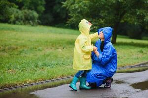 mamá y hijo en impermeables tener divertido juntos en el lluvia. concepto de familia vacaciones y contento infancia. foto