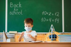 colegial en el salón de clases en un protector mascarilla. el concepto de enseñanza durante el epidemia foto