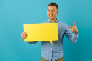 Handsome smiling man holding blank speech bubble sign isolated on light blue studio banner background with copy space photo