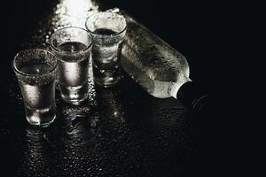 Cold vodka in shot glasses on a black background. Top view. Food background. photo