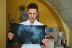 atractivo médico examinando un radiografía y sonriente a el cámara foto