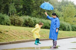 Mother and child, boy, playing in the rain, wearing boots and raincoats photo