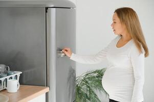 embarazada mujer a hogar en el cocina abre el refrigerador foto