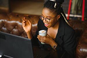 Attractive African American blogger with headphones and laptop communicating with followers in cafe photo