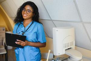 joven afro americano hembra médico en pie en clínica oficina cerca moderno ultrasonido máquina. foto