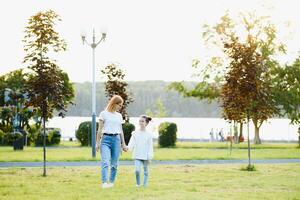 Attractive young woman with her little cute daughter are spending time together outdoors. Mom with daughter in park on a green grass during the sunset. photo