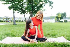 Mother and daughter doing yoga exercises on grass in the park at the day time photo