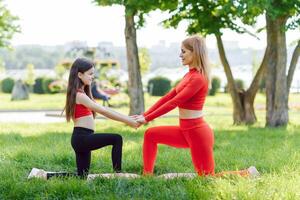 madre y hija haciendo yoga ejercicios en césped en el parque a el día tiempo. personas teniendo divertido al aire libre. concepto de simpático familia y de verano vacaciones. foto