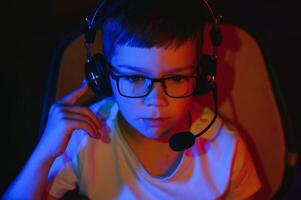 Child online broadcasts computer game, boy streams in headphones on rgb lighting background photo