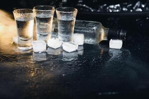 Close-up view of bottle of vodka with glasses standing on ice on black. photo
